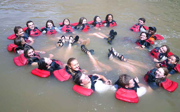 A group of students wearing life jackets float in a circle with their feet floating in the middle of the circle